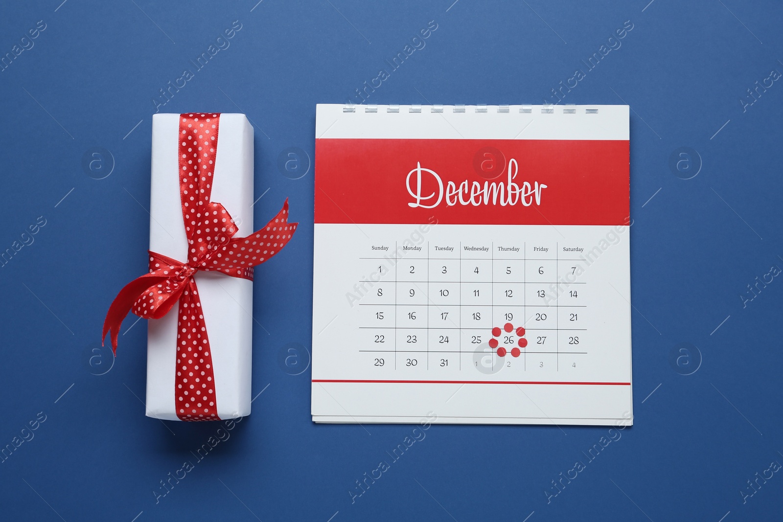 Photo of Calendar with marked Boxing Day date and gift on blue background, flat lay