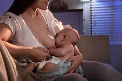 Photo of Young woman breastfeeding her little baby indoors at night, closeup
