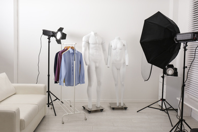 Photo of Ghost mannequins, clothes and professional lighting equipment in modern photo studio