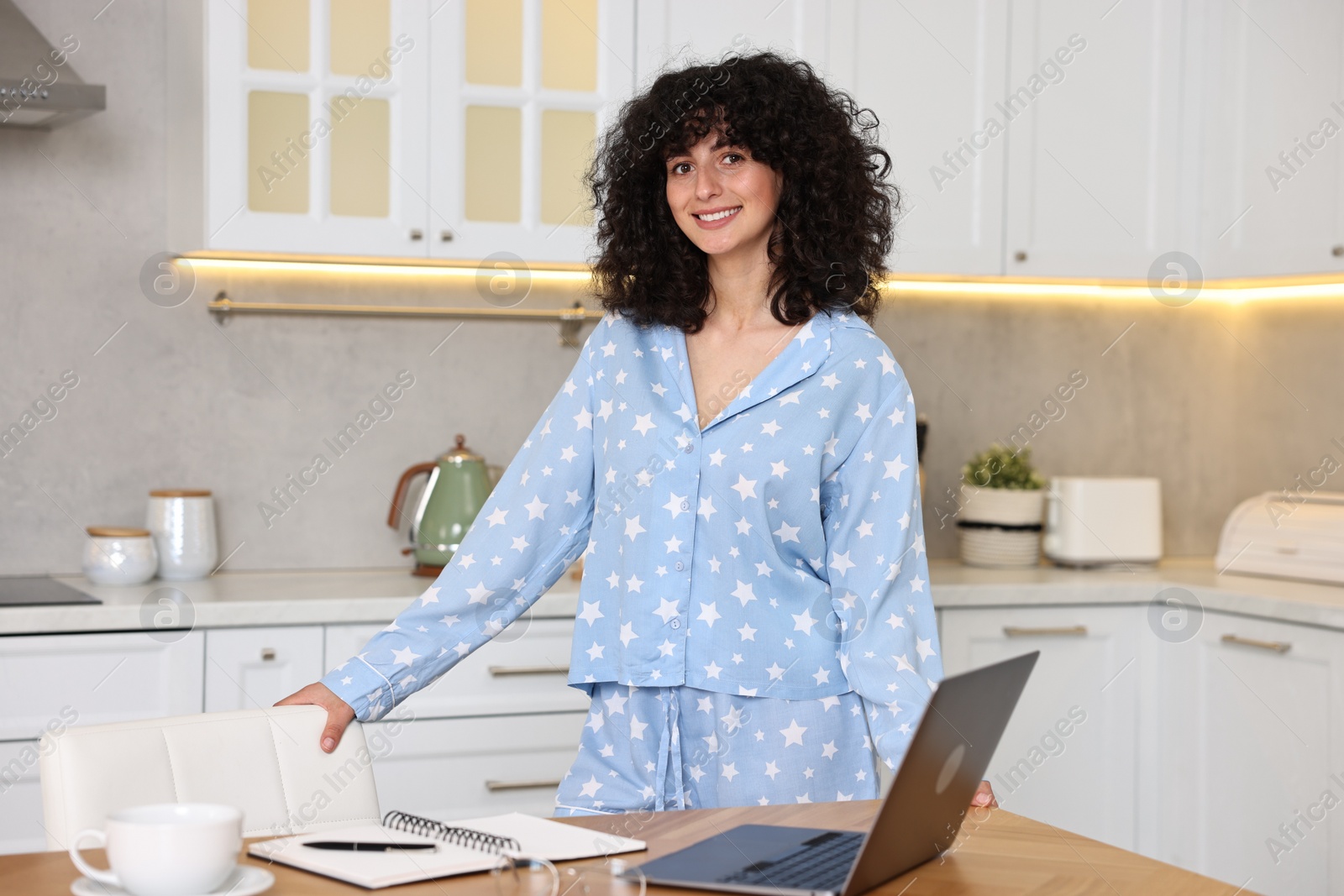 Photo of Beautiful young woman in stylish pyjama at wooden table in kitchen