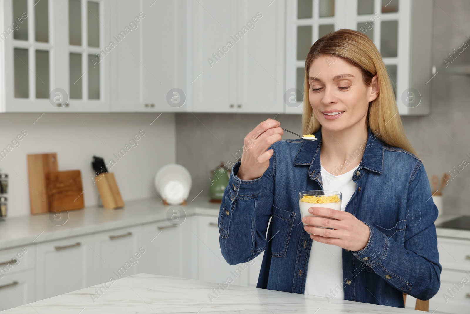 Photo of Woman eating tasty yogurt with spoon at table in kitchen. Space for text