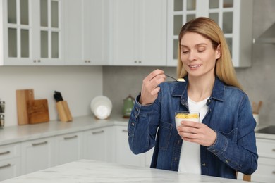 Photo of Woman eating tasty yogurt with spoon at table in kitchen. Space for text