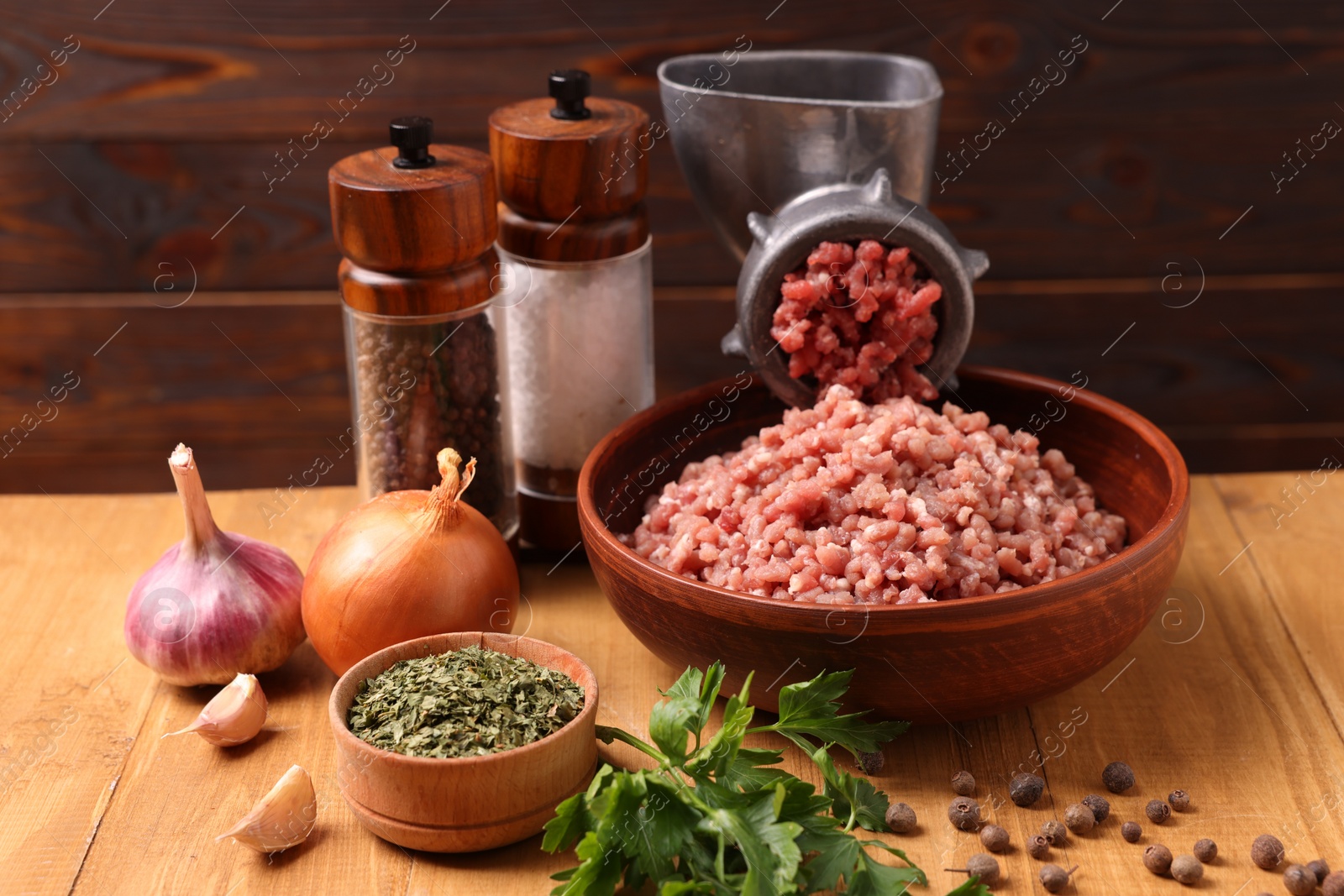 Photo of Manual meat grinder with beef mince, spices and parsley on wooden table