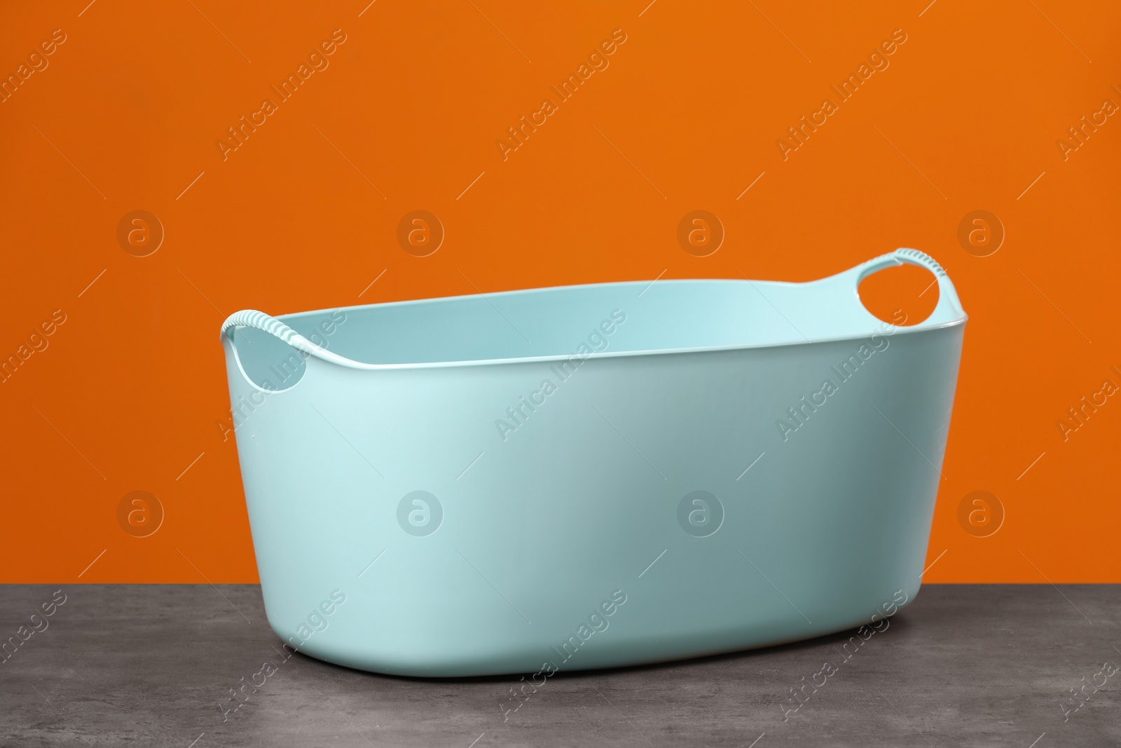 Photo of Empty plastic laundry basket near orange wall