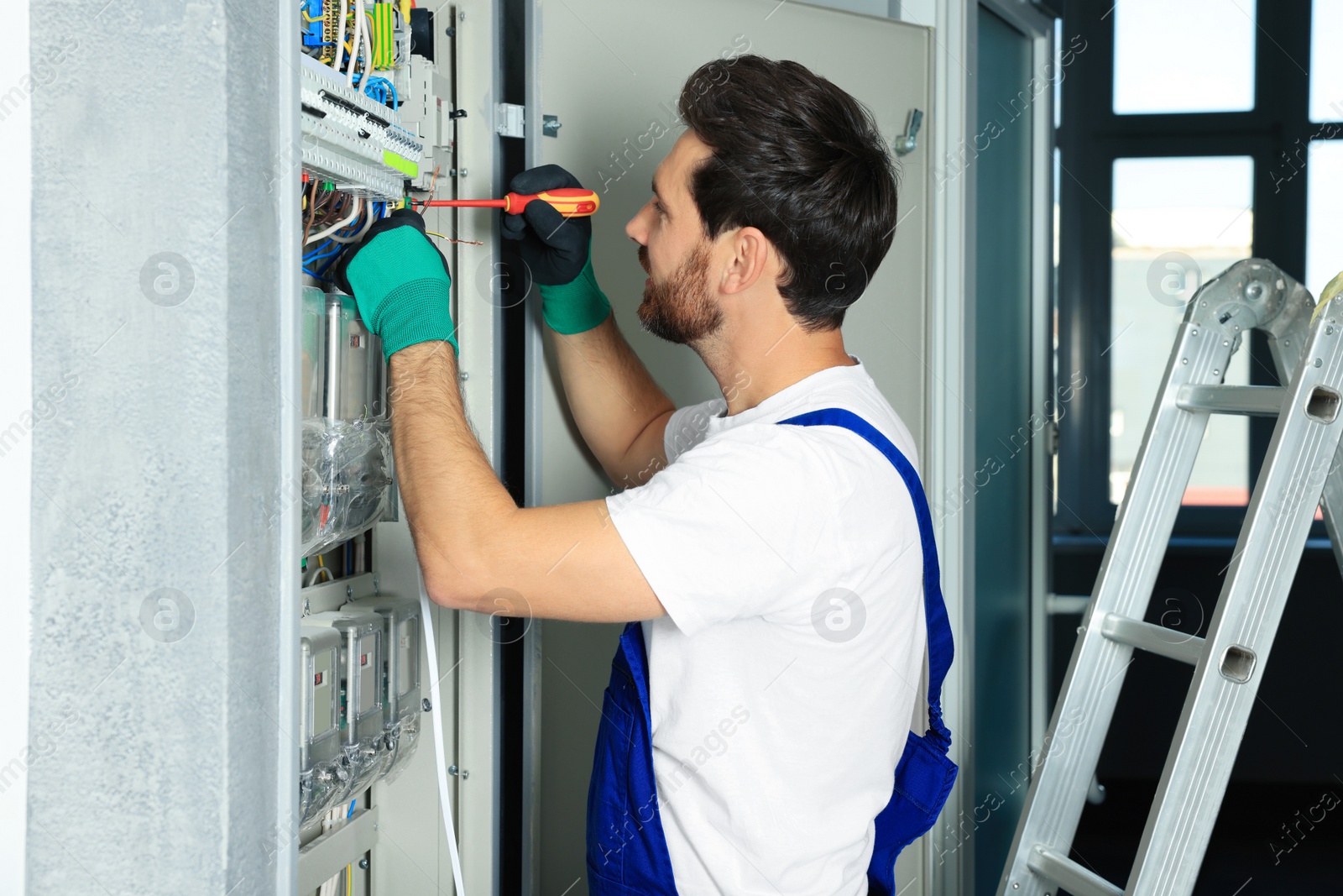 Photo of Electrician repairing fuse box with screwdriver indoors
