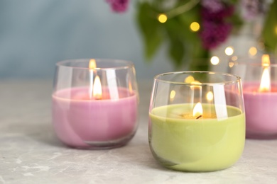 Photo of Burning candles in glass holders on grey table against blurred lights