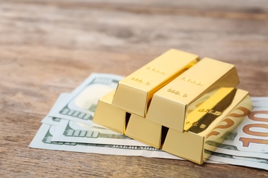 Photo of Gold bars and dollar bills on wooden table. Space for text