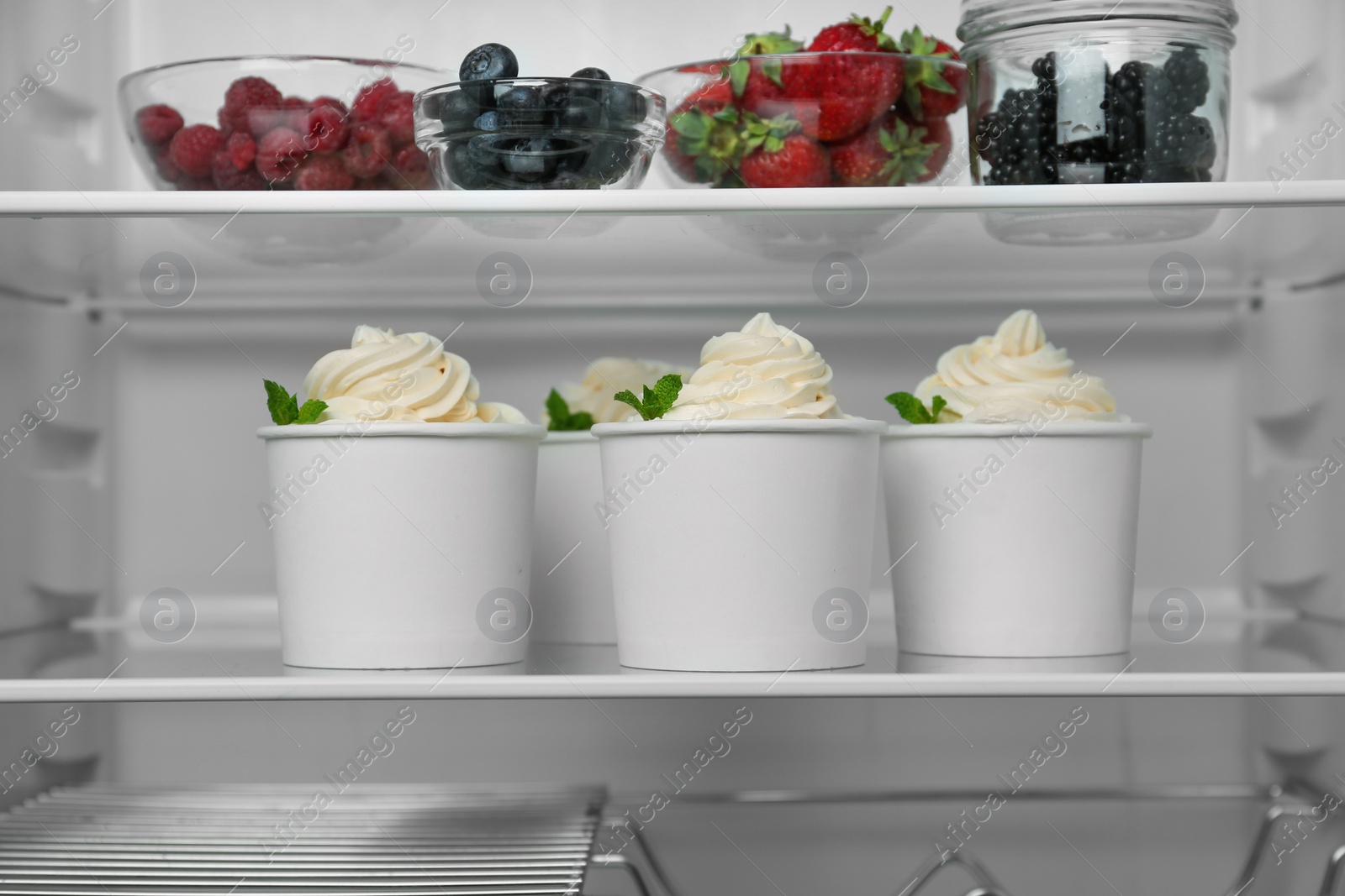 Photo of Cups with tasty frozen yogurt on fridge shelf