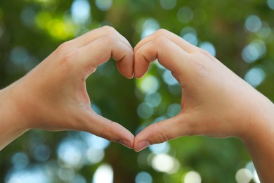 Man making heart with hands outdoors on sunny day, closeup