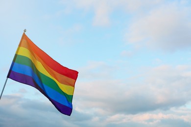 Photo of Bright LGBT flag against blue sky with clouds. Space for text