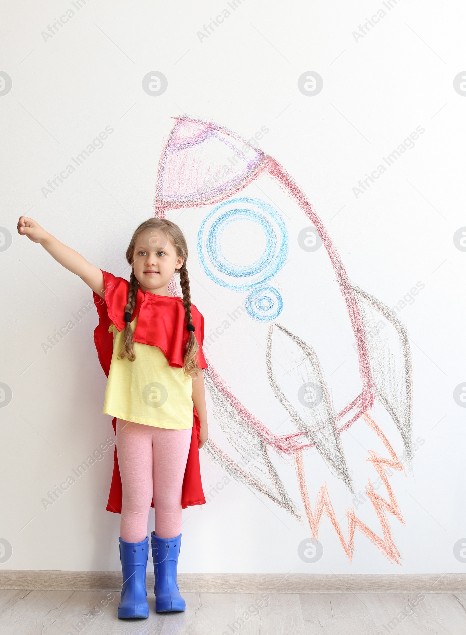 Photo of Adorable little child playing astronaut near wall with drawing of spaceship indoors