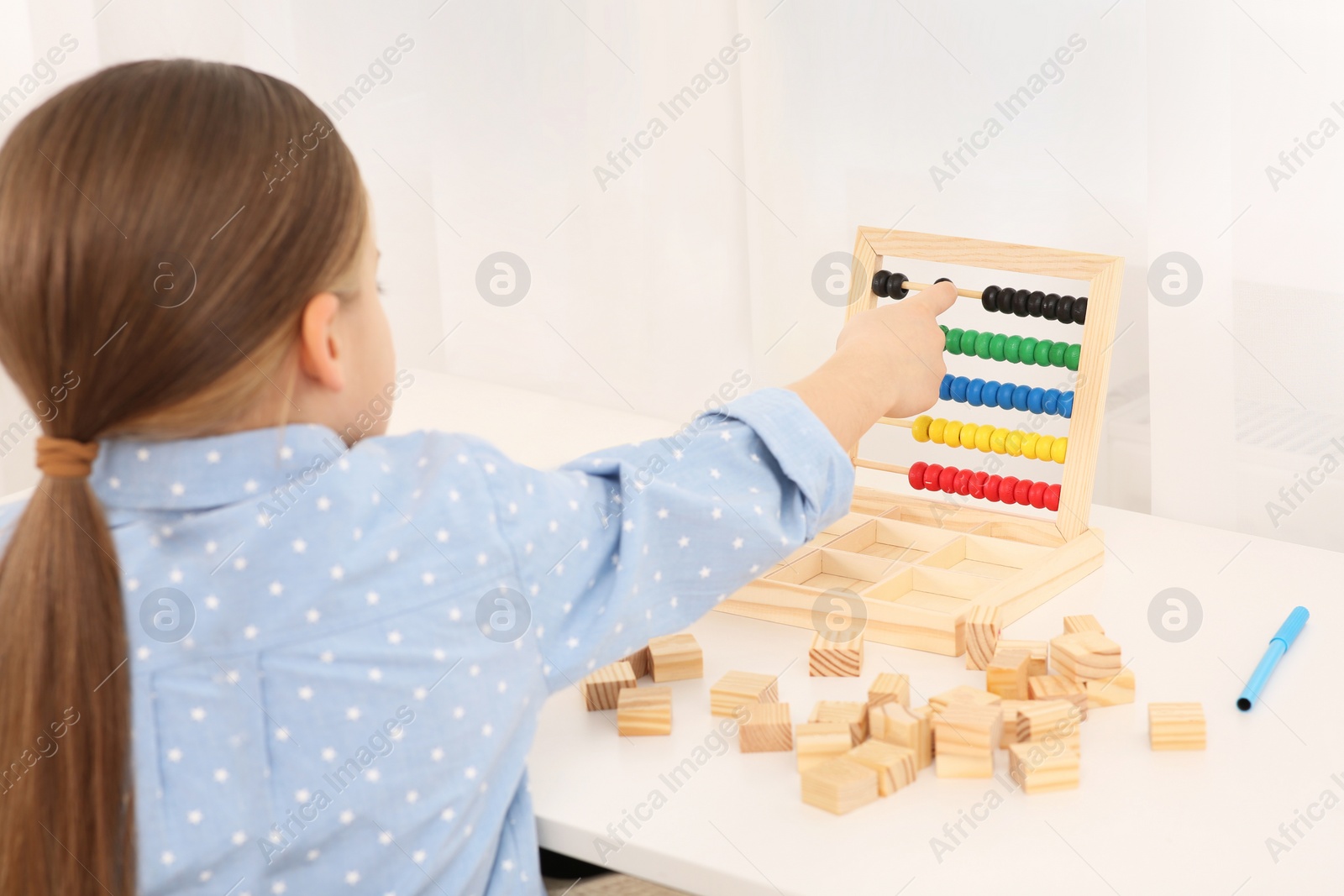 Photo of Girl playing with colorful wooden abacus at desk in room. Home workplace