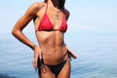 Photo of Sexy young woman in stylish bikini on seashore, closeup. Space for text