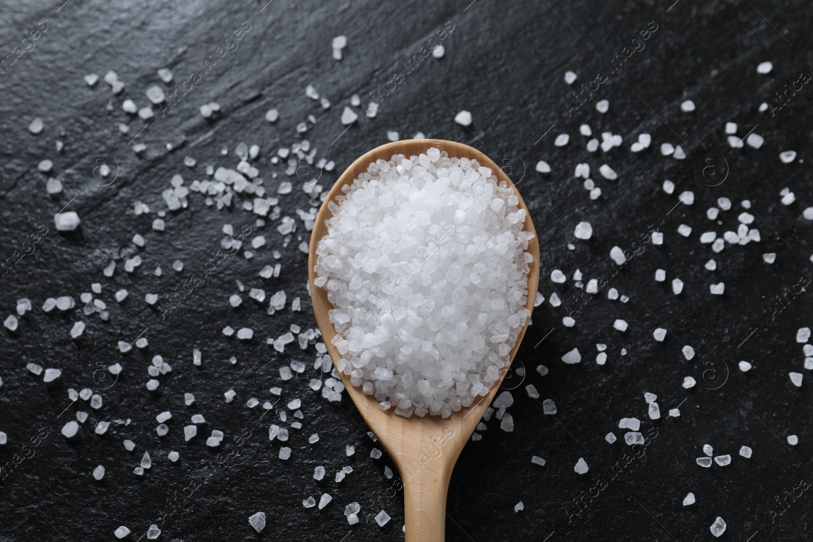 Photo of Organic white salt and spoon on black table, top view