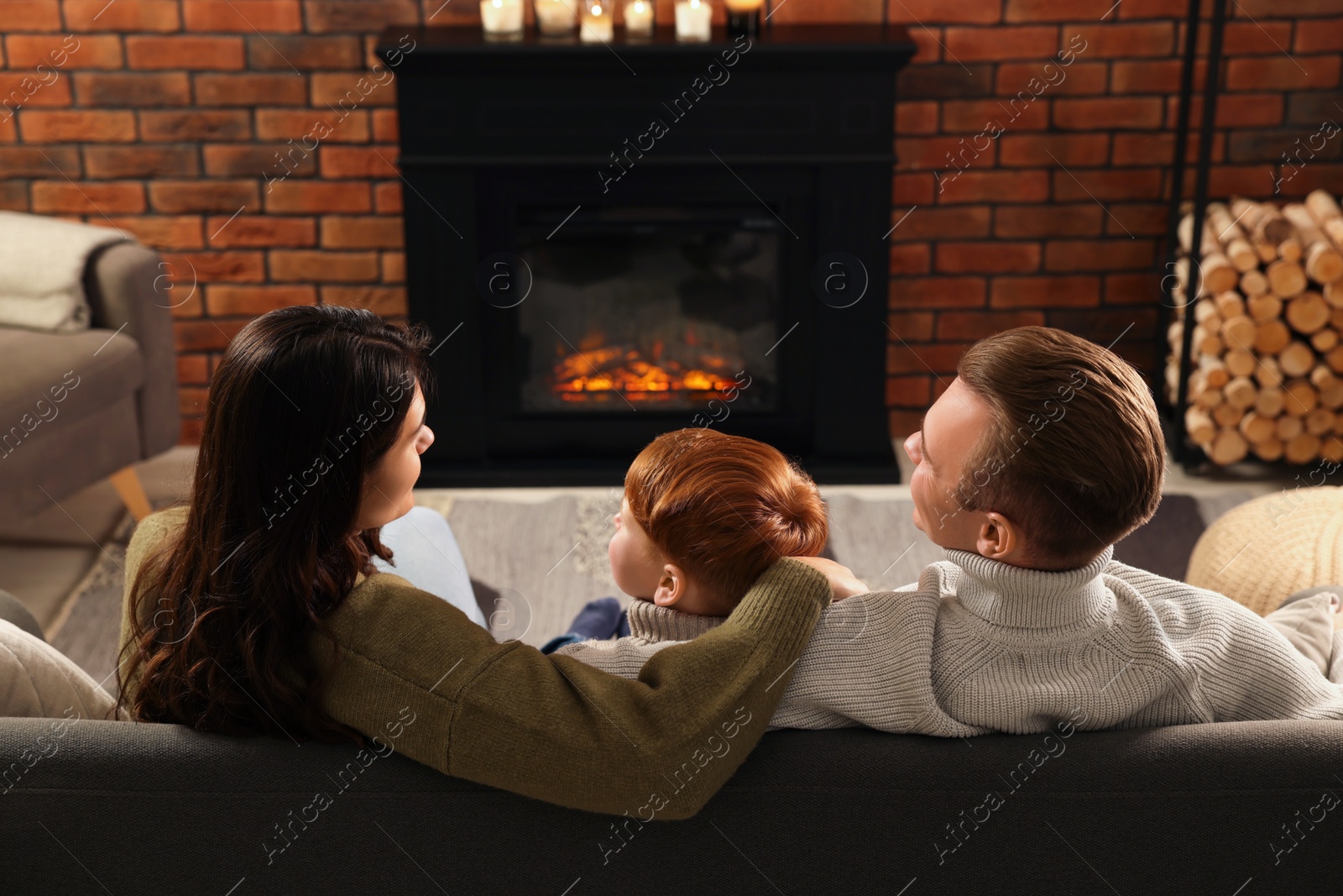 Photo of Family spending time together on sofa near fireplace at home, back view