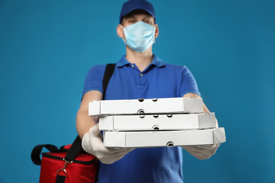 Photo of Courier in protective mask and gloves holding pizza boxes on blue background. Food delivery service during coronavirus quarantine