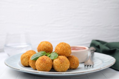 Photo of Plate of delicious fried tofu balls with basil and sauce on white tiled table