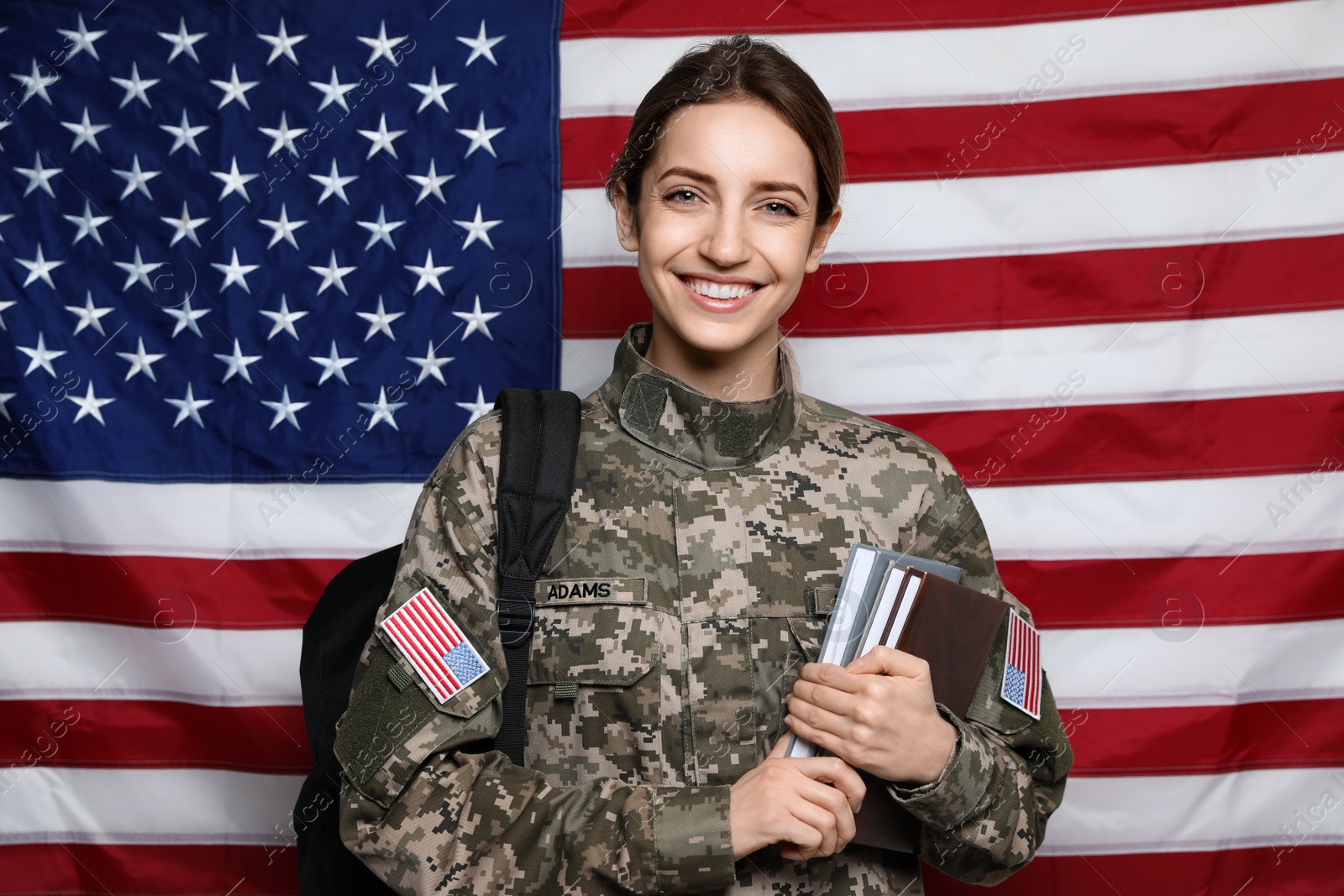 Photo of Female cadet with backpack and books against American flag. Military education