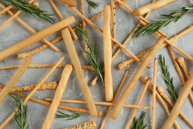 Photo of Delicious grissini sticks and rosemary on grey marble table, flat lay