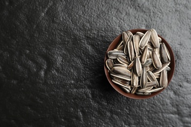 Photo of Raw sunflower seeds in bowl on black background, top view. Space for text