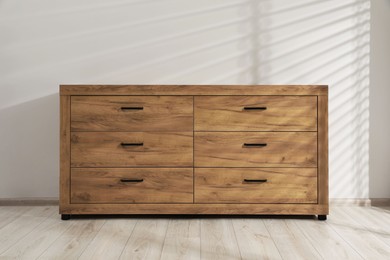 Wooden stylish chest of drawers near white wall indoors