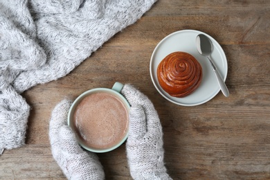 Photo of Woman with delicious cocoa drink and hot bun at wooden table, top view