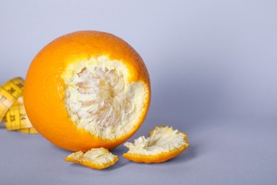 Photo of Cellulite problem. Orange and measuring tape on light grey background, closeup. Space for text