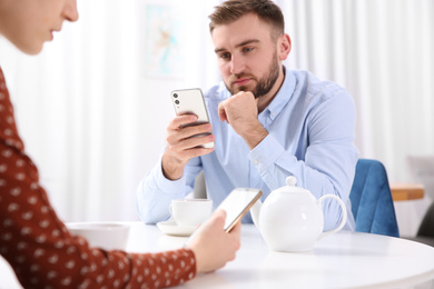 Photo of Couple addicted to smartphones ignoring each other in cafe. Relationship problems