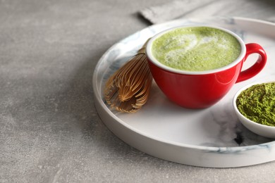 Cup of tasty matcha latte, green powder and bamboo whisk on light gray table, space for text