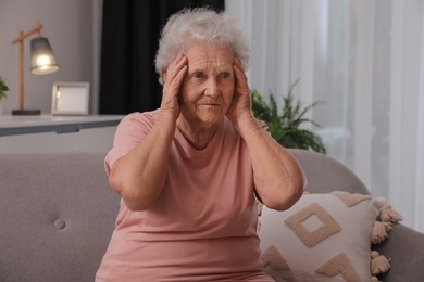 Photo of Senior woman with headache sitting on sofa at home
