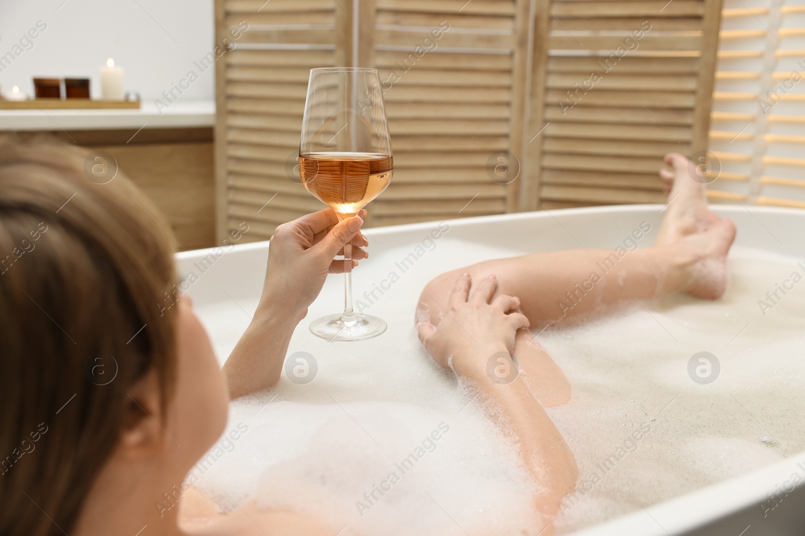 Photo of Woman with glass of wine taking bath in tub indoors, closeup