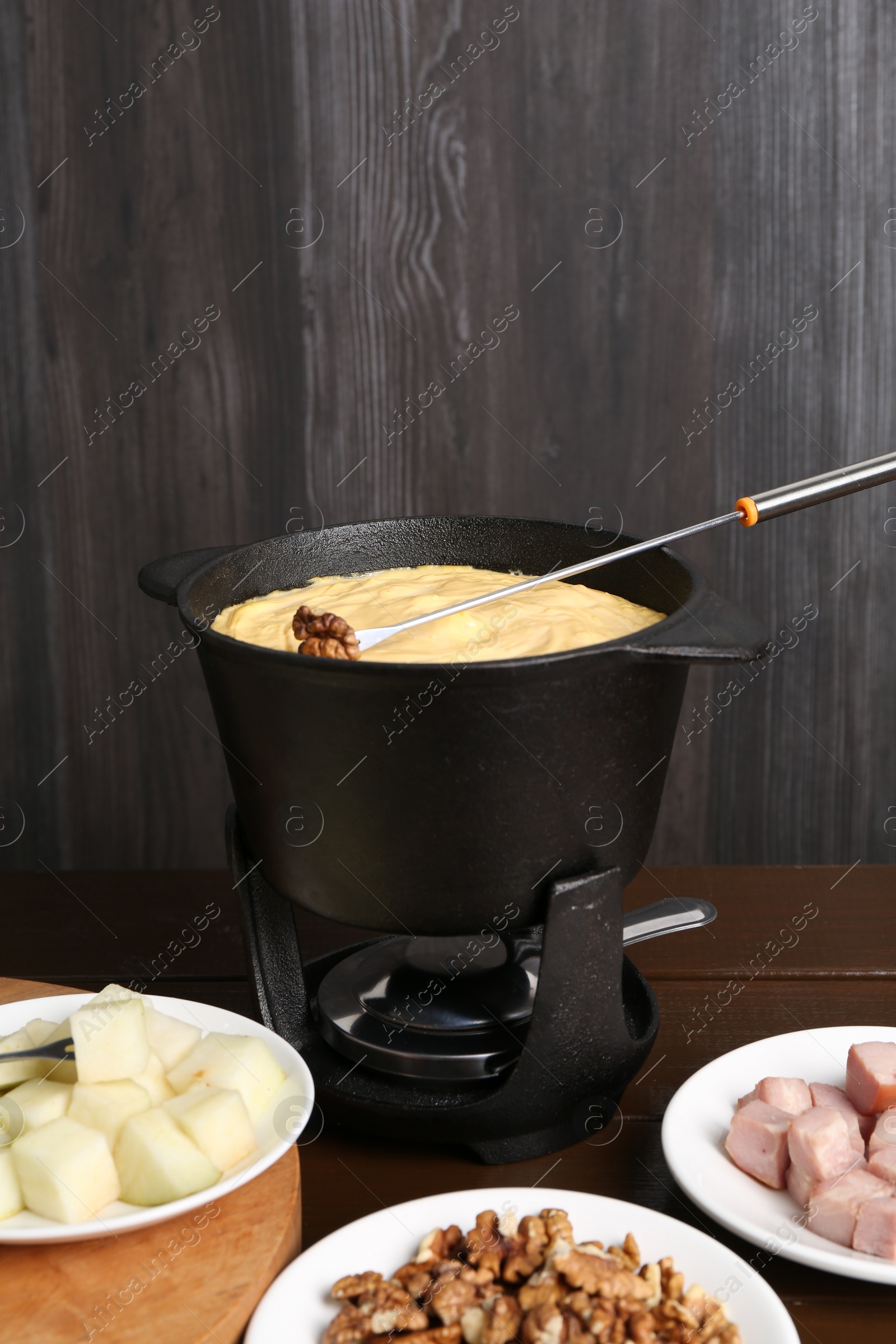 Photo of Fondue pot with tasty melted cheese, fork and different snacks on wooden table