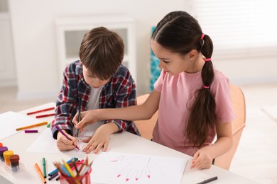 Photo of Happy brother and sister drawing at white table in room