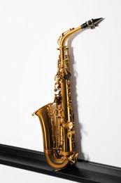 Photo of Beautiful saxophone on shelf near white wall. Musical instrument