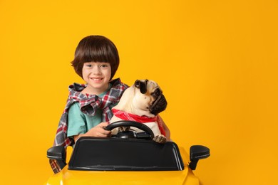 Little boy with his dog in toy car on yellow background