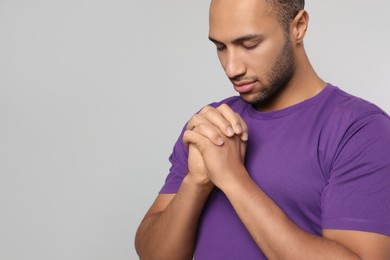 African American man with clasped hands praying to God on light grey background. Space for text