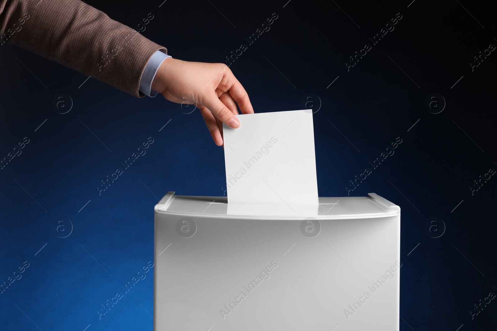 Photo of Woman putting her vote into ballot box on dark blue background, closeup