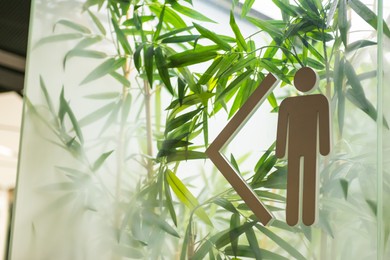 Photo of Public toilet sign for gentlemen on glass behind beautiful plants, closeup