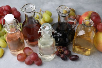 Photo of Different types of vinegar and fresh fruits on grey table