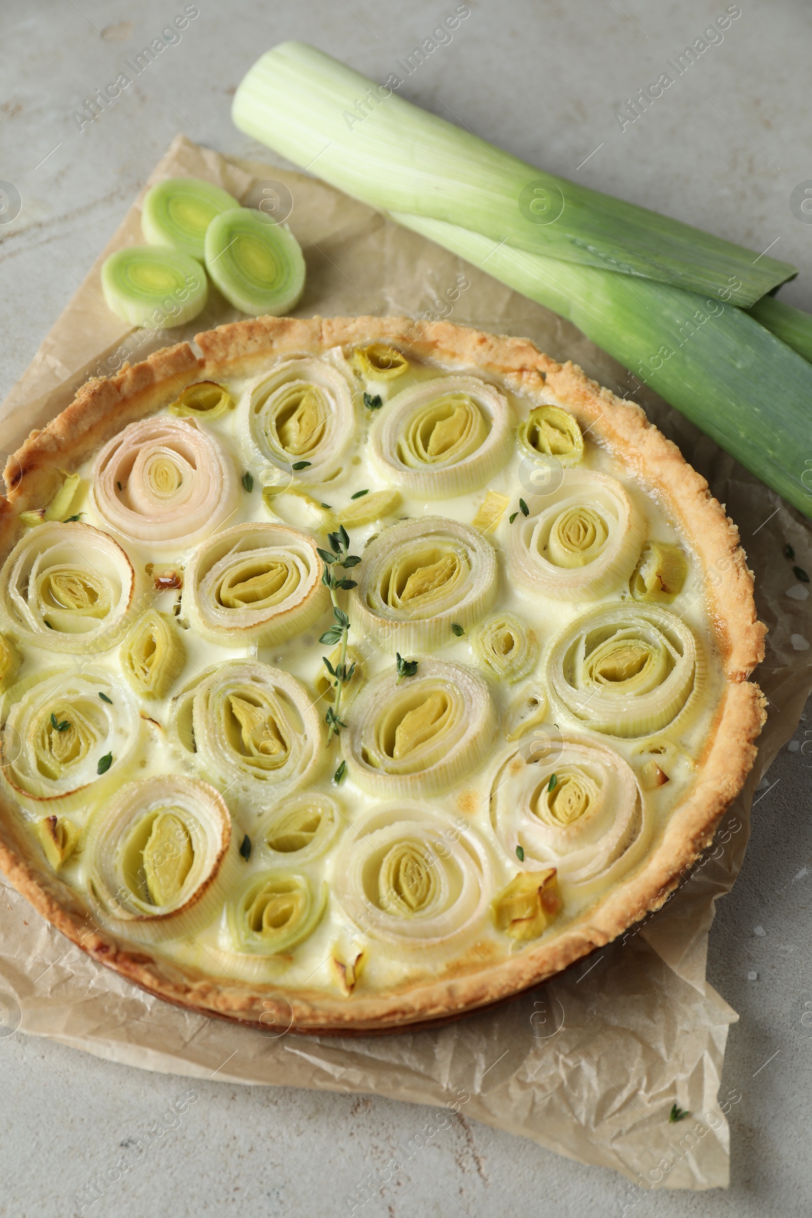 Photo of Tasty leek pie and fresh stalk on grey textured table, above view