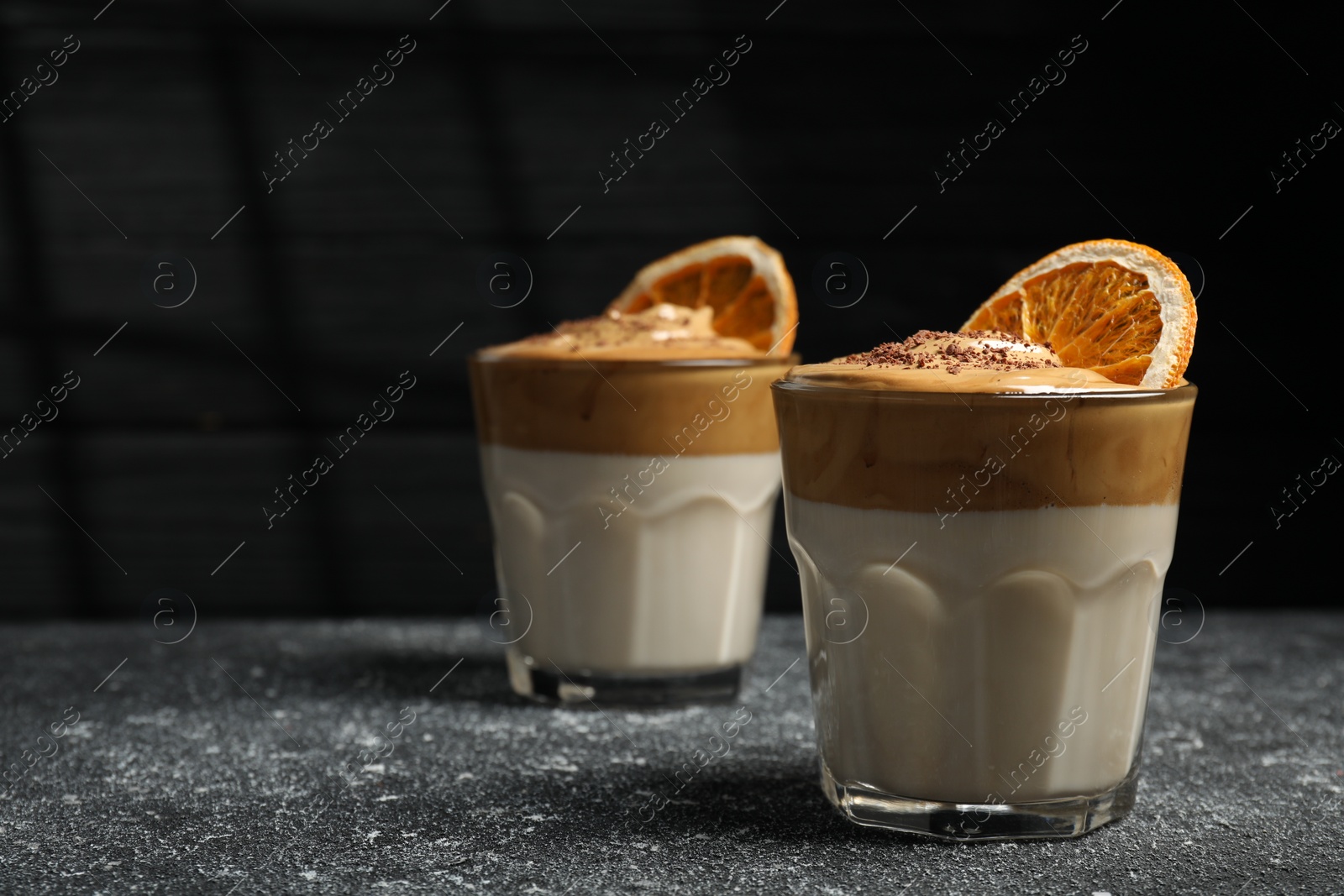 Photo of Glasses of delicious dalgona coffee with dry orange and chocolate on grey textured table, space for text