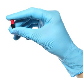 Scientist in protective gloves holding pill on white background, closeup