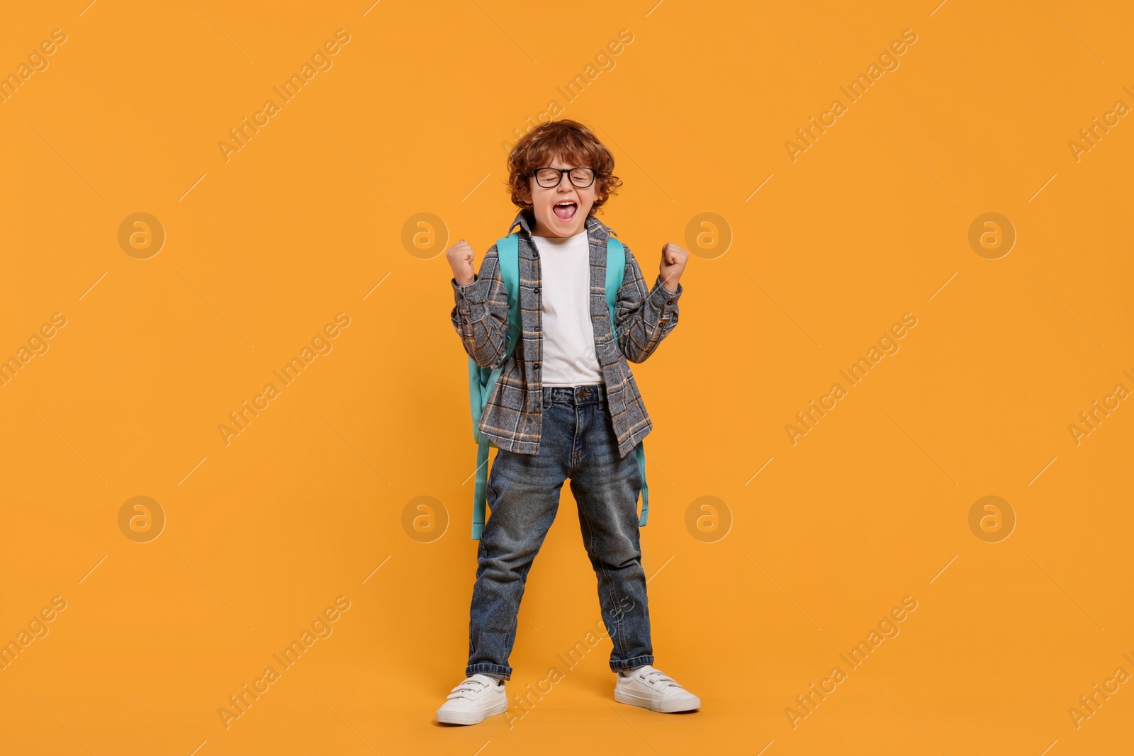 Photo of Emotional schoolboy with backpack on orange background