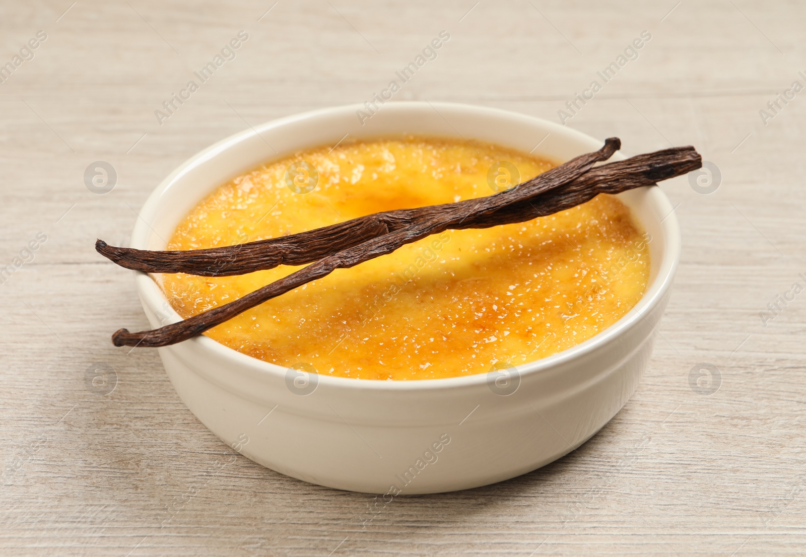 Photo of Delicious creme brulee and vanilla sticks on white wooden table, closeup view