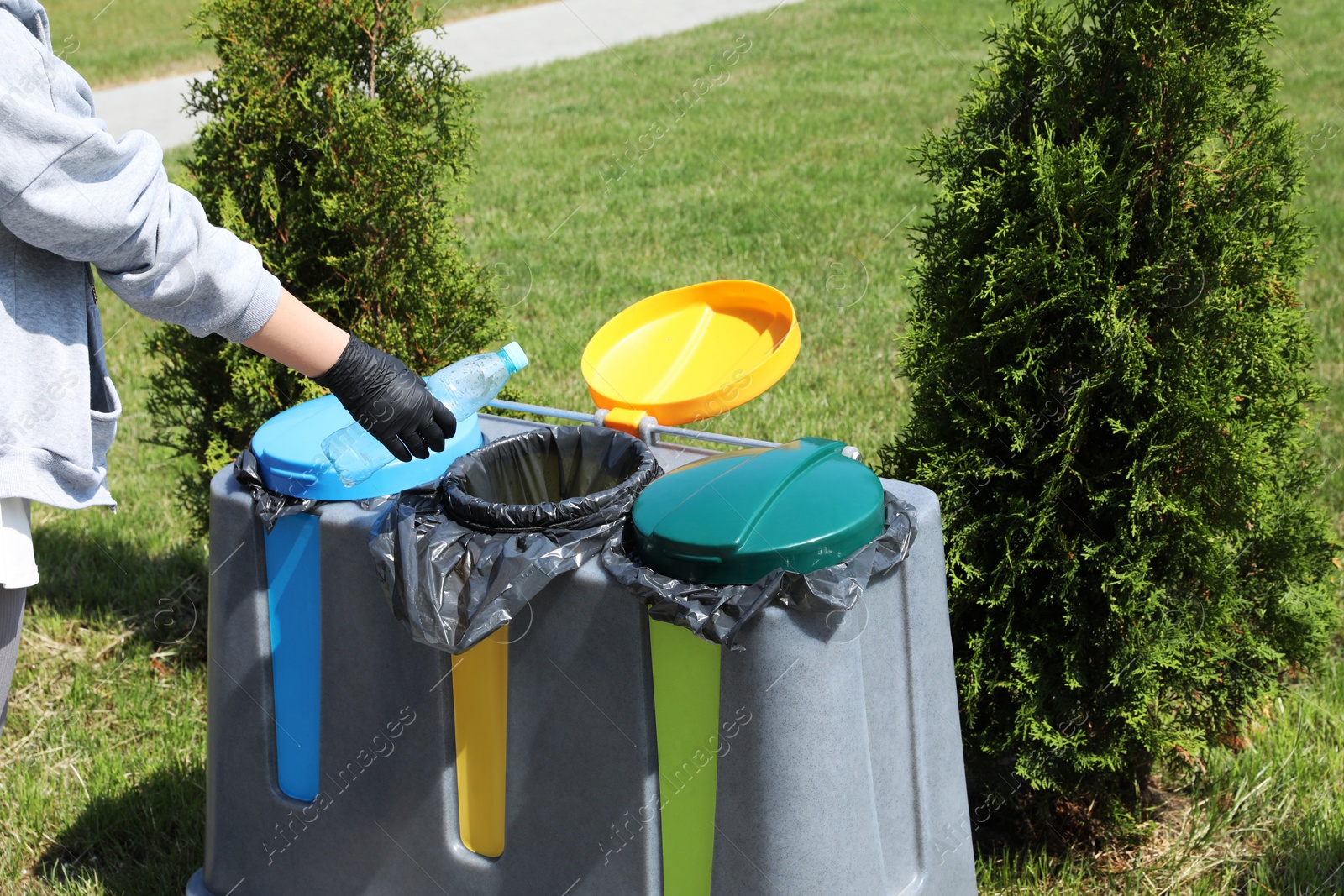 Photo of Woman throwing plastic bottle in bin outdoors, closeup. Recycling concept