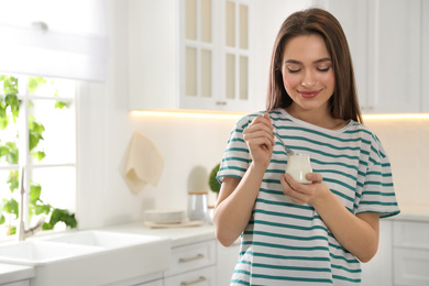 Young attractive woman with tasty yogurt in kitchen. Space for text