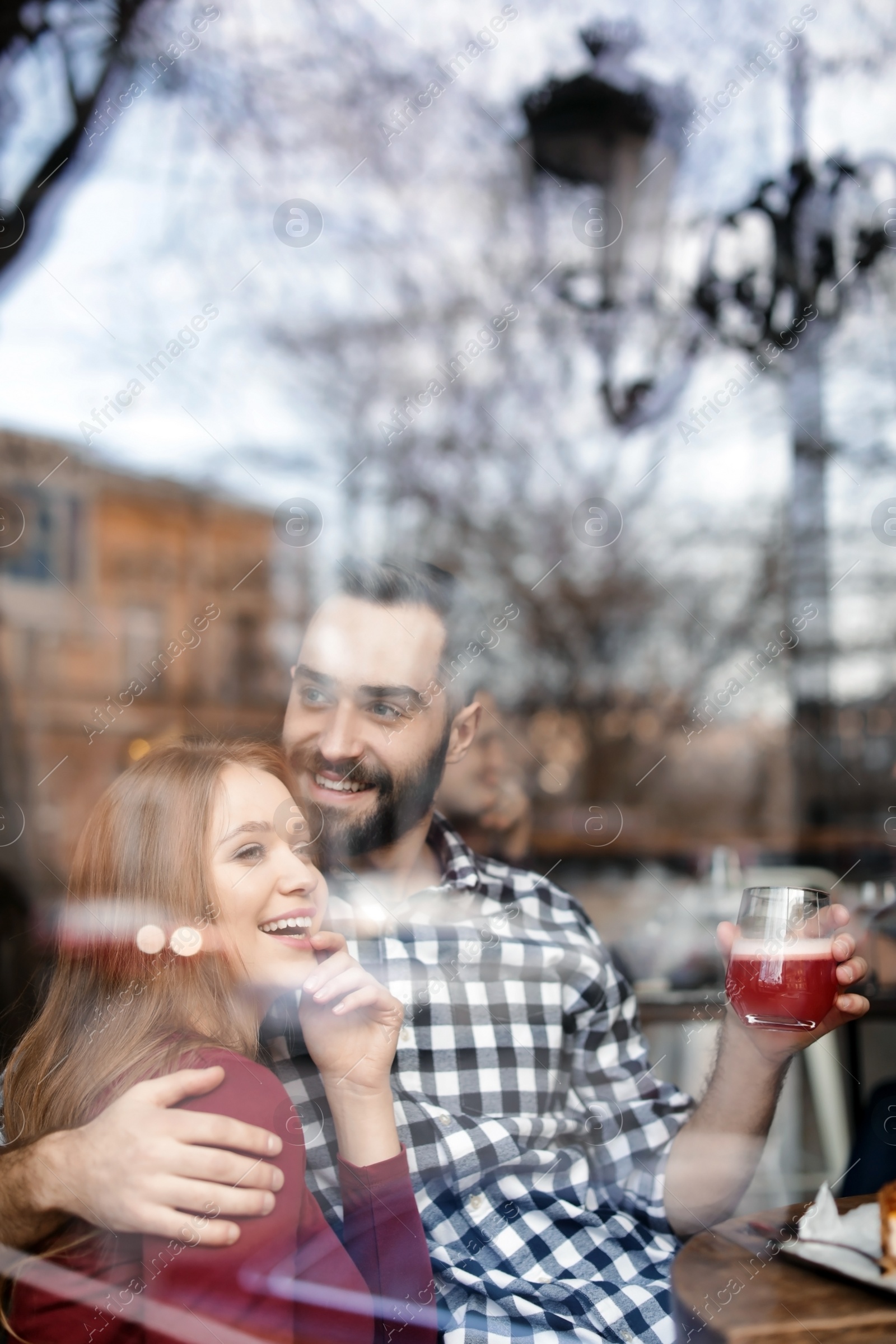 Photo of Lovely young couple spending time together in cafe, view from outdoors through window