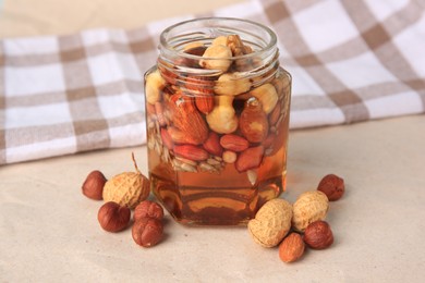 Photo of Jar with different nuts and honey on beige table