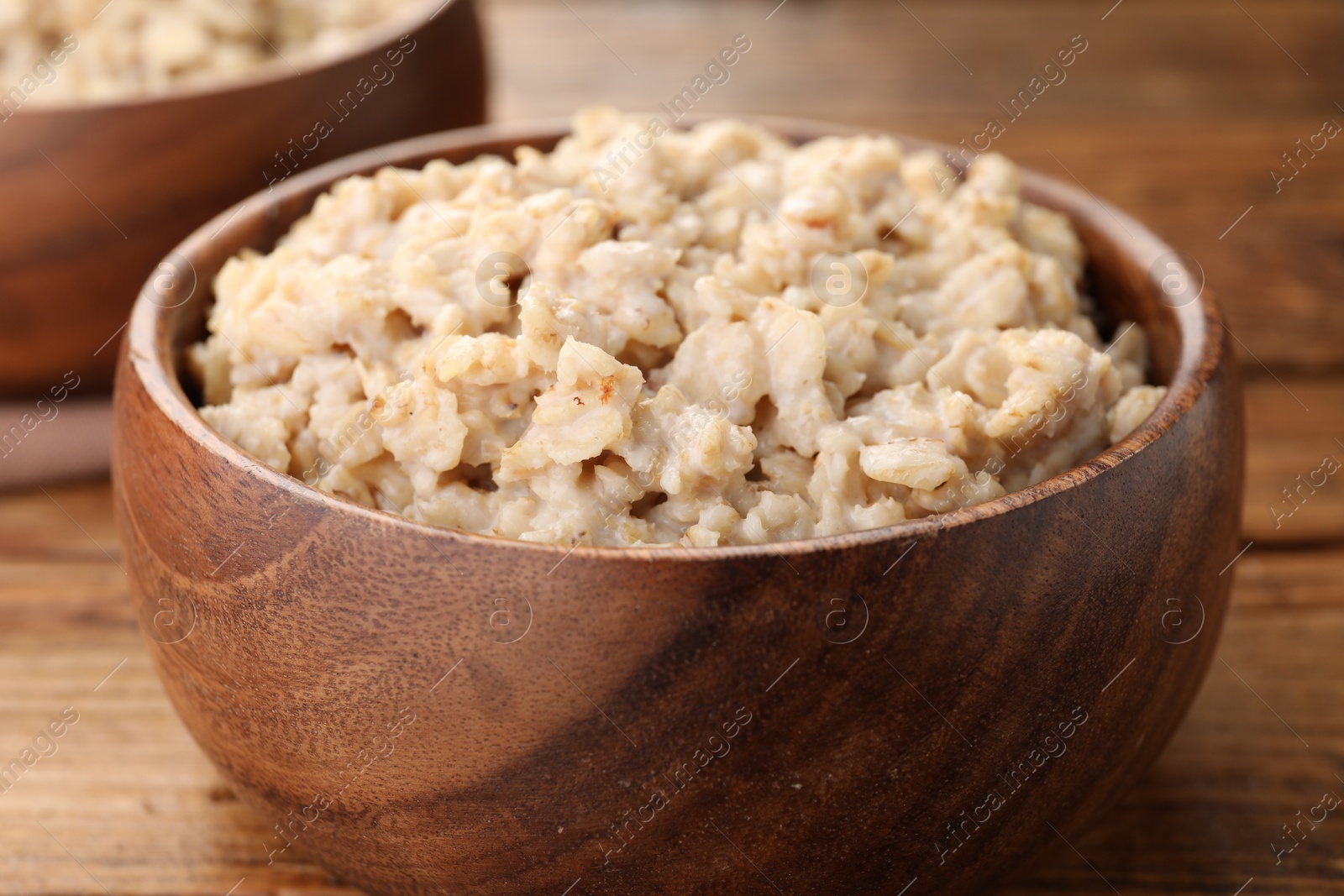 Photo of Tasty boiled oatmeal in bowl on wooden table, closeup