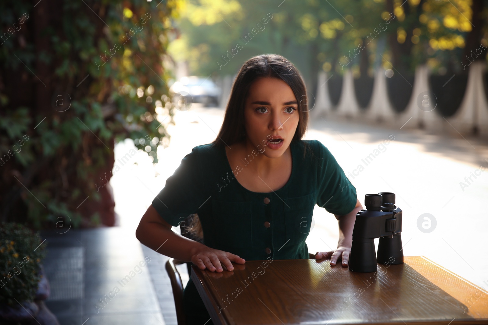 Photo of Jealous woman with binoculars spying on ex boyfriend in outdoor cafe